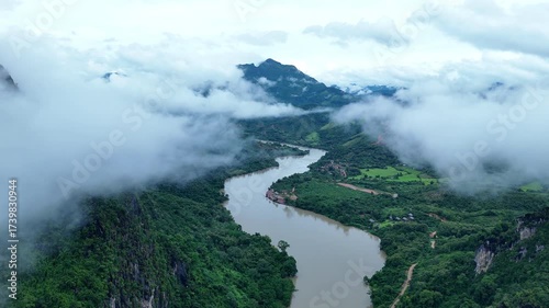 A breathtaking aerial view of Nong Khiaw, Laos, surrounded by towering limestone mountains, winding rivers, and soft morning mist drifting through the valley, creating a stunning and tranquil natural 