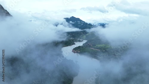 A breathtaking aerial view of Nong Khiaw, Laos, surrounded by towering limestone mountains, winding rivers, and soft morning mist drifting through the valley, creating a stunning and tranquil natural 