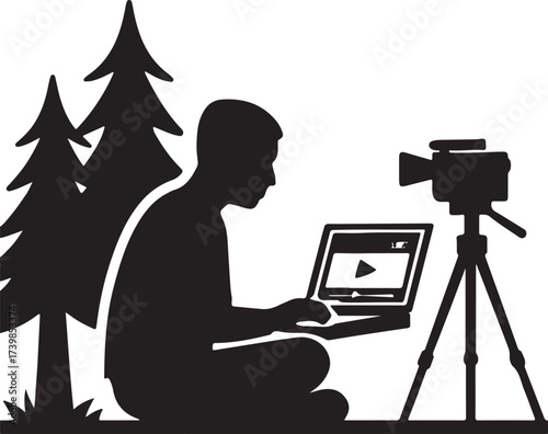 Silhouette of a person working on a laptop outdoors with a video camera on a tripod nearby