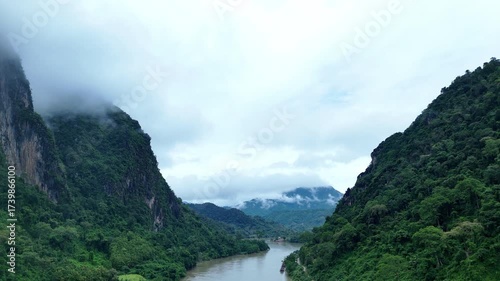 A breathtaking aerial view of Nong Khiaw, Laos, surrounded by towering limestone mountains, winding rivers, and soft morning mist drifting through the valley, creating a stunning and tranquil natural 