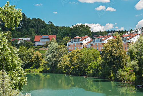 Wallpaper Mural Row of riverside homes backed by lush greenery reflecting in calm river under bright clouds and deep blue summer sky in Slovenia Torontodigital.ca