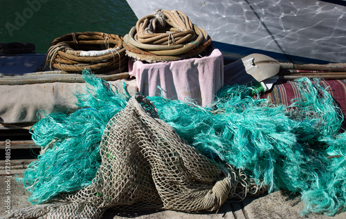 Fishing gear on a dock near water: coiled ropes, turquoise net, pink towel, and striped mat. Rich textures and maritime colors evoke a vivid coastal atmosphere. Horizontal outdoor composition.
