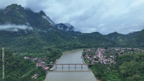 A breathtaking aerial view of Nong Khiaw, Laos, surrounded by towering limestone mountains, winding rivers, and soft morning mist drifting through the valley, creating a stunning and tranquil natural 