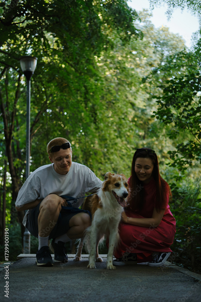 Obraz premium Happy couple crouching and petting their dog on a forest path. Outdoor activity with pets and love.