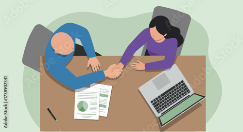 Overhead view of two people shaking hands over a desk, documents, and laptop.
