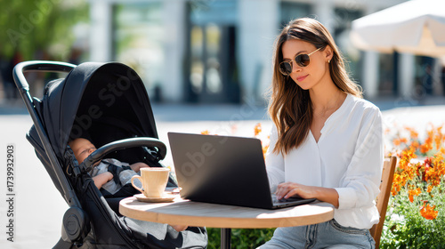 Woman working on a laptop at a café with a baby stroller beside her, enjoying a sunny day surrounded by flowers