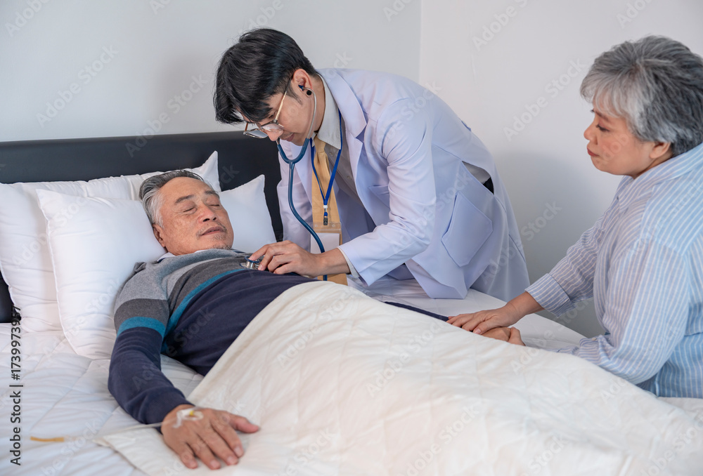 Fototapeta premium scene of elderly man patient lying on bed getting examine from a doctor,and his wife encourage beside
