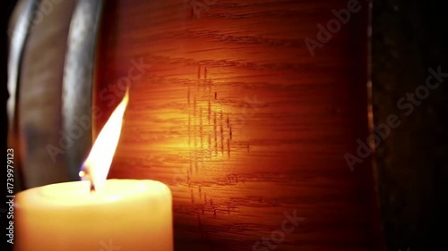 A single burning candle casts a warm, flickering glow on a dark, textured wooden surface.