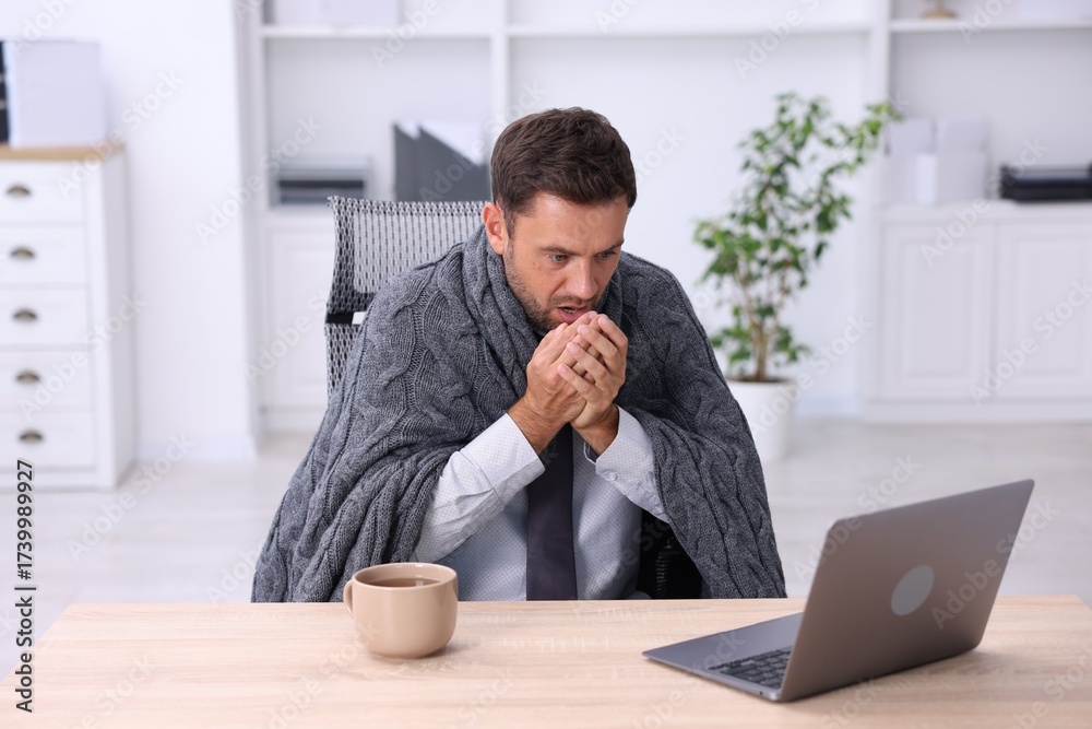 Naklejka premium Air conditioning. Man with blanket suffering from cold temperature at workplace in office