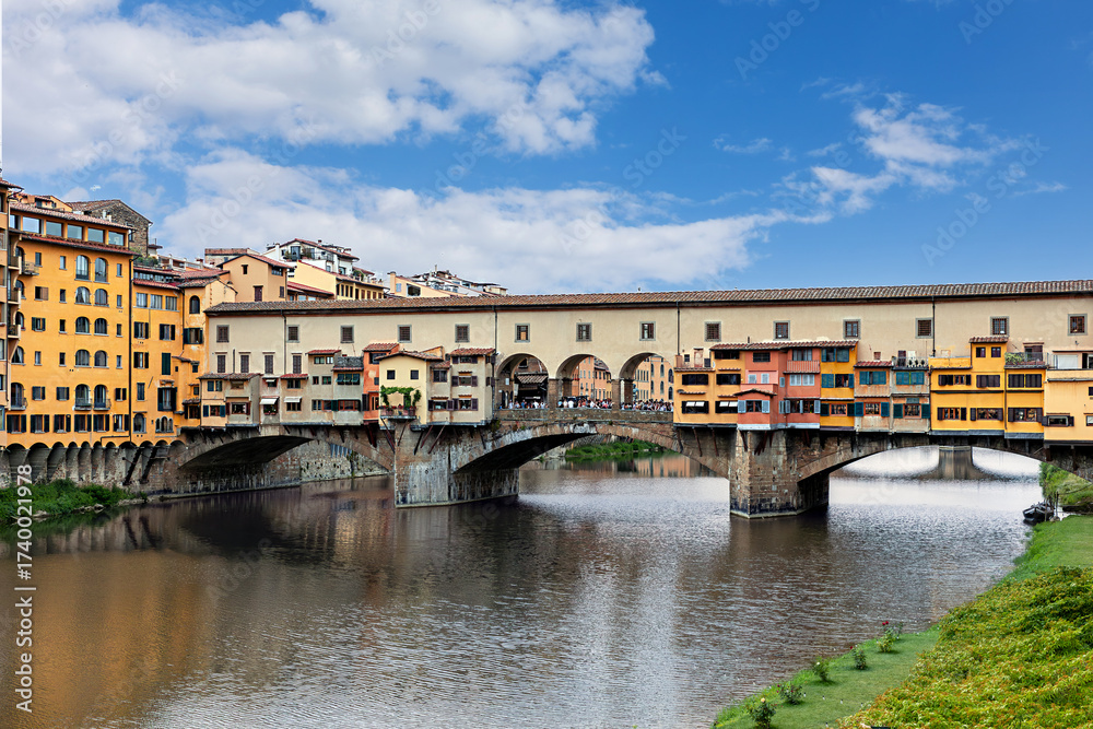 Obraz premium The Ponte Vecchio bridge in Florence showcases its colorful buildings and shops reflecting in the tranquil waters Arno river.
