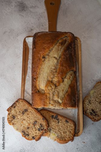 Freshly baked banana bread is sliced and displayed on a wooden cutting board. The bread has a golden-brown crust and chocolate chips, perfect for a cozy snack at home.
