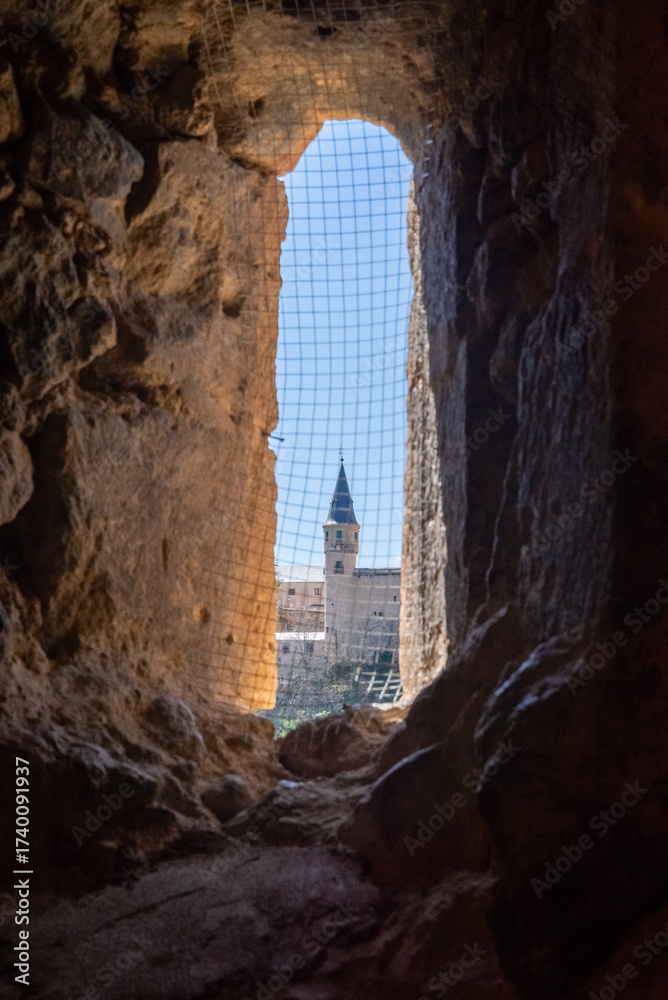 Obraz premium View from the Templar Church tower near Segovia, Spain. The Alcázar is dramatically framed through a dark stone embrasure, contrasting medieval walls and a clear blue sky.