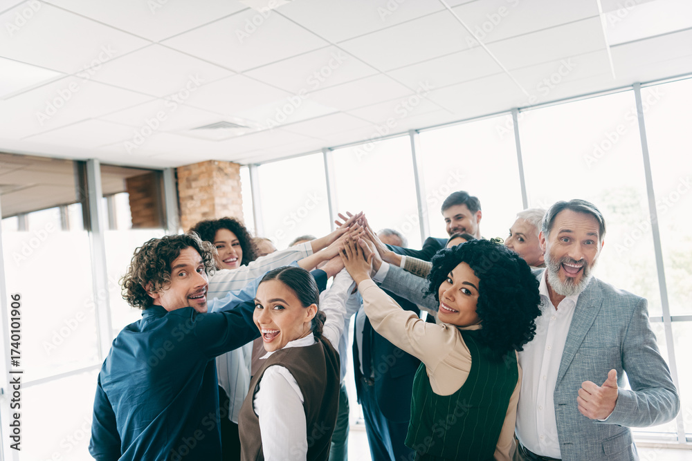 Obraz premium Group of professionals celebrating teamwork with a high-five gesture in a modern office environment