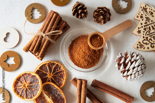 Ground cinnamon and cinnamon sticks with orange slices and pine cones on a white background