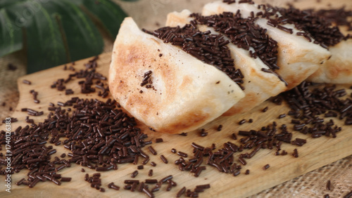 Fotografia Close-up of sliced, sweet martabak, a pancake-like dessert, topped with chocolate sprinkles, displayed on a wooden board with a green leaf