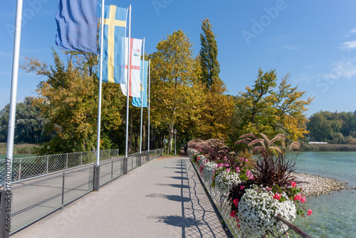 The entrance bridge to Mainau Island on Lake Constance, adorned with colorful flags, floral arrangements, and golden autumn foliage on a bright