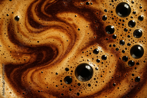 Closeup of coffee foam with dark swirling patterns and bubbles on surface.