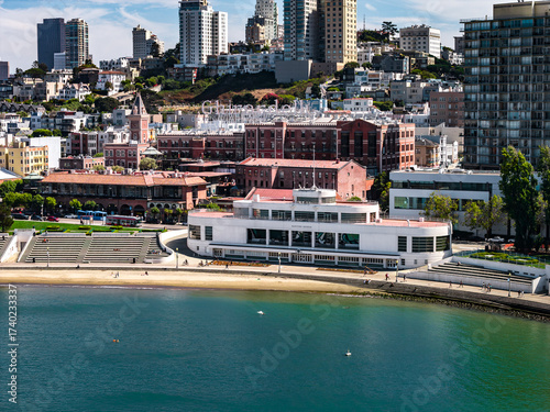 Photography Aerial view of San Francisco featuring the Art Deco Aquatic Park Bathhouse, curved beach, tiered seating, cityscape, and vibrant blue green water