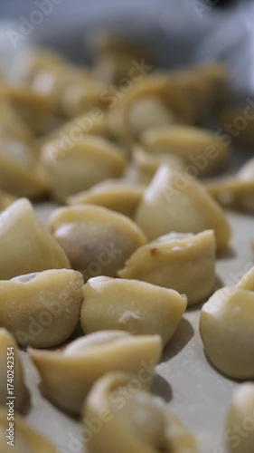 Close-up view of fresh, raw, handmade tortellini arranged on a tray, ready for cooking. Traditional italian cuisine concept showing the delicate preparation of authentic filled pasta. Vertical video