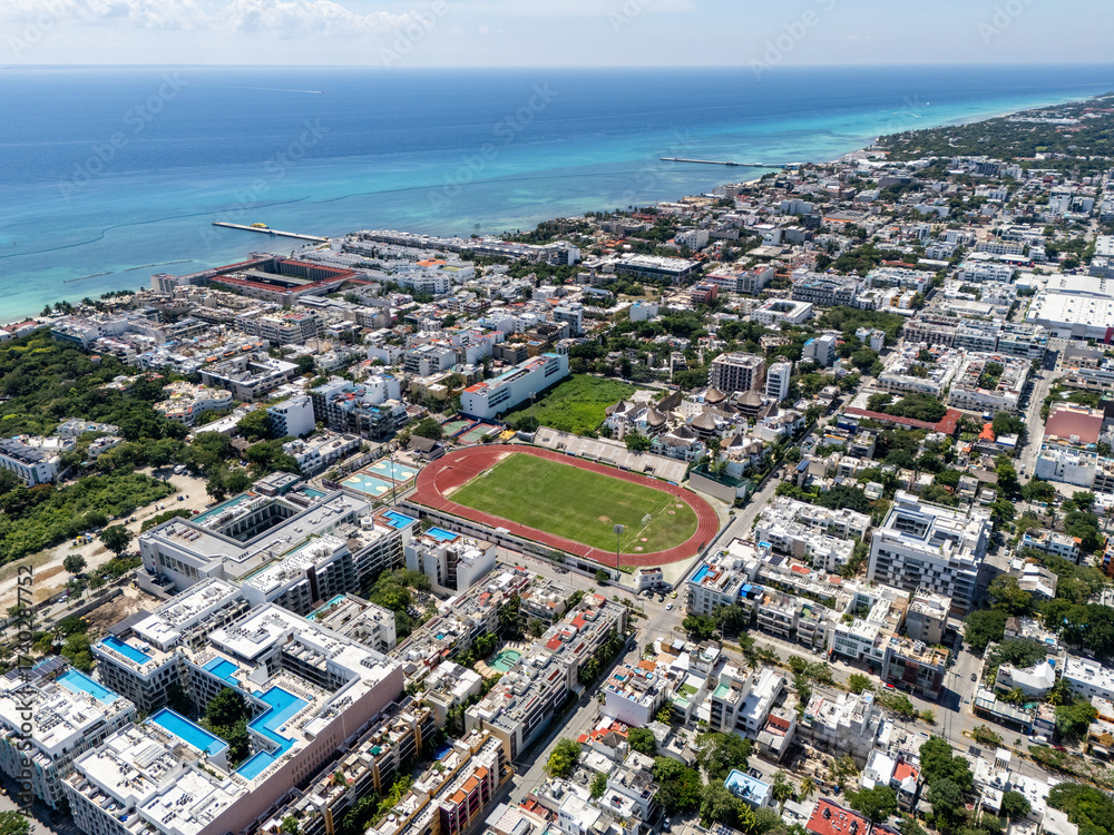 Fototapeta premium Aerial drone view of downtown area in Playa del Carmen with buildings and stadium and blue Caribbean Sea in the background on a summer day
