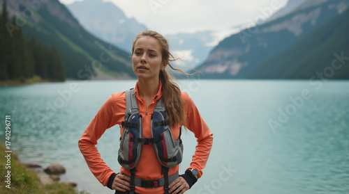 Female trail runner resting by alpine lake with hydration vest