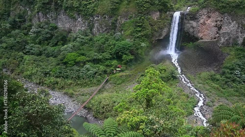 Bride's Cloakl Falls, La Cascada de la Novia, Banos de Agua Santa, Ecuador. Majestic waterfall cascades down rocky cliff surrounded by lush greenery and flowing river in serene natural landscape