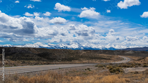 Desert Road Leading to Snow-Capped Mountains Under Partly Cloudy Sky, Nevada in Spring