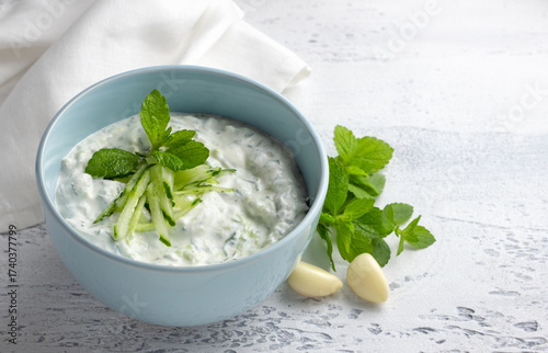 Fresh traditional Greek tzatziki sauce with yogurt, cucumber and mint light blue ceramic bowl on light background. Healthy Mediterranean appetizer, dip or dressing
