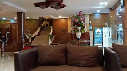 A cozy hotel lobby in the early morning, softly illuminated by warm sunlight streaming through large windows. The atmosphere feels calm and welcoming, with comfortable sofas, elegant décor, and fresh 