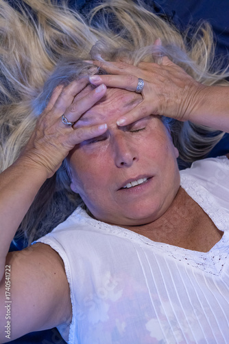 Adult woman with blond hair with an expression of annoyance, pain, or stress holding her head