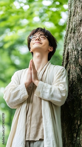 Young adult man resting against tree and praying for hope and healing in nature