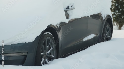 Snow covered electric car parked on street. Challenges and nuances of operating car and charging battery in winter. Preparing to drive after heavy snowfall.