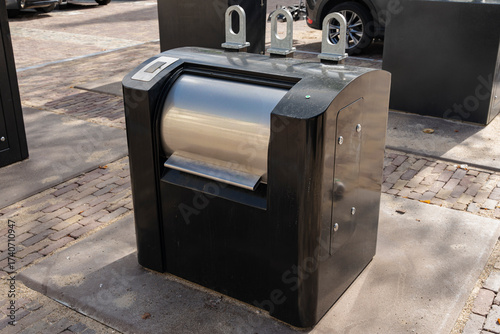 Automated public waste bin: A modern black receptacle featuring a cylindrical stainless steel opening.