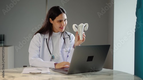 Female doctor is making a report on female genitalia in laptop computer, holding model of the female reproductive system gynecologist, Report on Ovarian and Cervical cancer, Cervix disorder