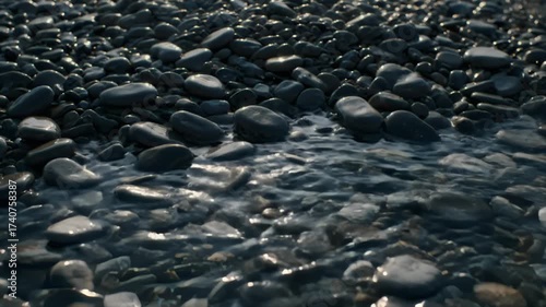 Gentle ocean waves washing over dark, smooth beach pebbles.