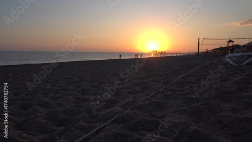 A Serene Sunset Over the Tranquil Beach: Witness the Radiant Sky Gradually Transitioning from Golden Hues to Twilight as Visitors Enjoy the Peaceful Seaside Atmosphere