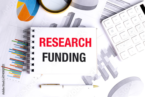 Notebook with text research funding on financial documents with calculator and pen on white desk