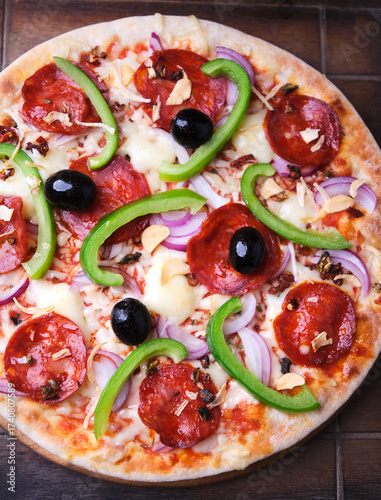Pizza with chorizo ​​sausage, mozzarella cheese, green pepper and black olives. Rustic wooden background. Soft focus.	