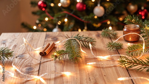 Rustic Christmas Table with Pine Branches, Cinnamon, and String Lights in Front of Decorated Tree