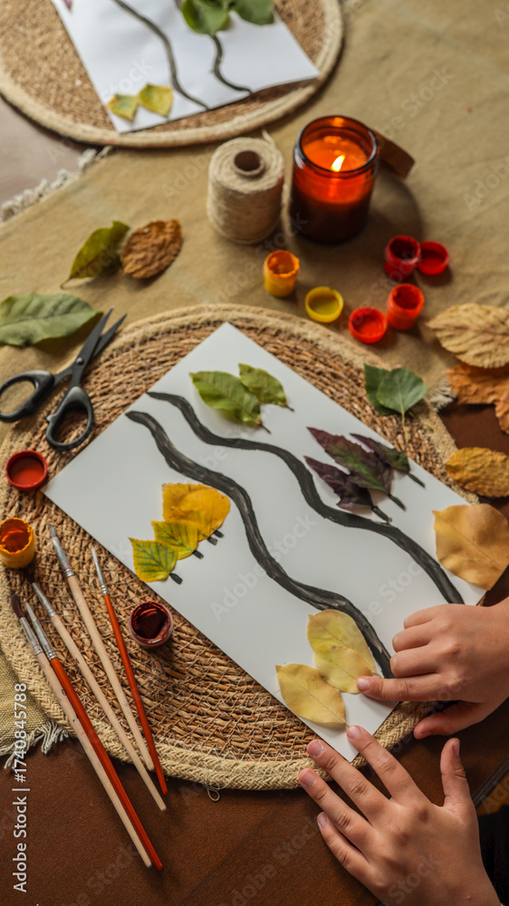 Fototapeta premium Autumn leaf art project with a lit candle and craft supplies.