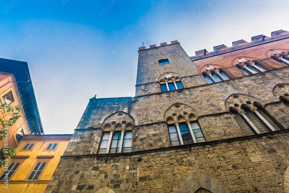 Naklejka premium Image of historic center in Siena featuring grand medieval buildings, monumental stone and brick facades, cultural landmarks and authentic Italian old town atmosphere
