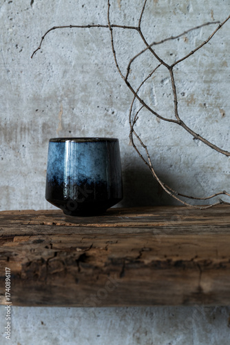 Dark ceramic cup on rustic wood with dry branch against concrete wall, minimal wabi sabi still life with natural textures.