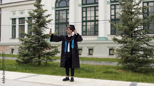 Modern graduate boy with cap and gown. Young man talks online with parents and friends to show them moments from the graduation ceremony for students who successfully graduated from university