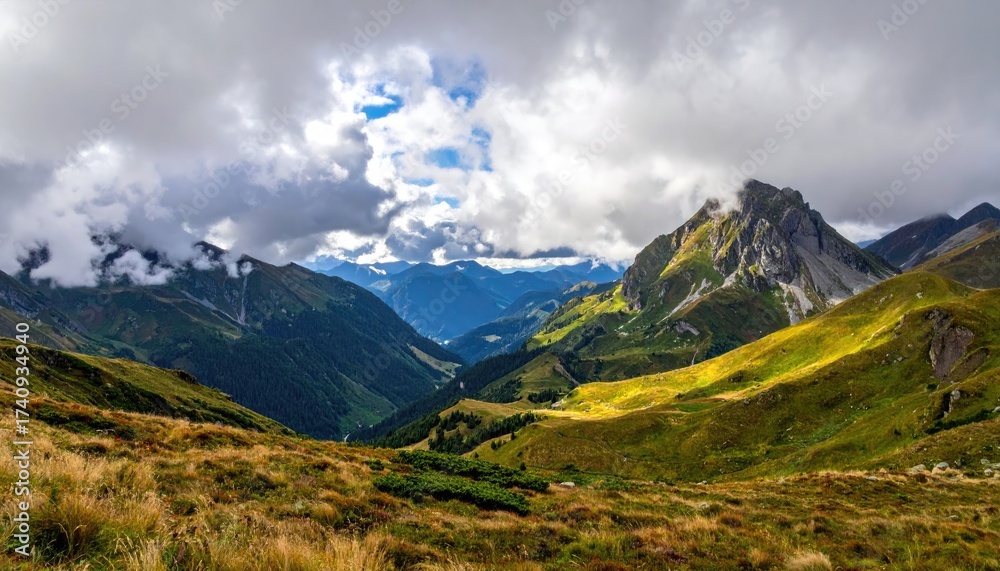 Naklejka premium Scenic Mountain Valley Under Dramatic Cloudy Sky Landscape with Green Slopes and Distant Peaks in Warm Natural Light