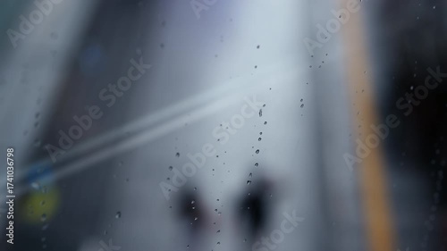 Rain drops on the window and people walking in the rain in the background