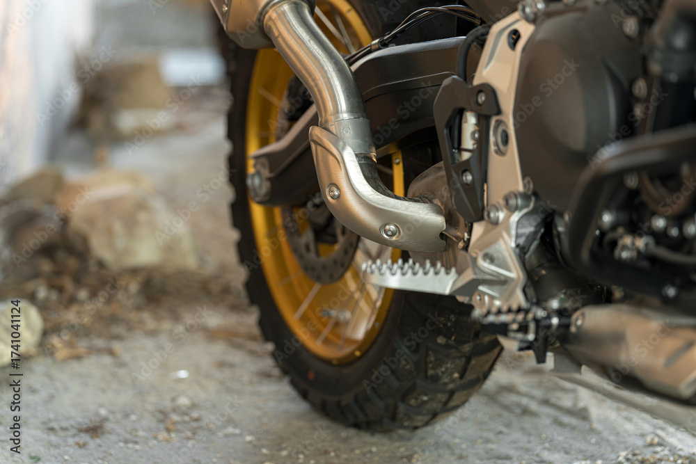 Fototapeta premium Close-up view of motorcycle exhaust and tire on a rugged surface in a garage setting
