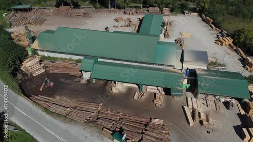 Aerial view of a sawmill factory in the mountains surrounded by dense forest, with stacks of processed lumber and timber. Wood industry and natural resource production	