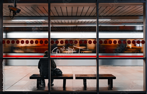 A solitary traveler at Prague's Vyšehrad station during early morning hours. Quiet atmosphere, minimalistic composition with emphasis on light and shadow.