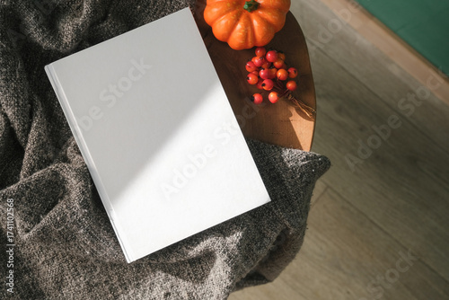High angle view of white hard cover book on wooden decorative table with a pumpkin and red berries