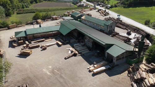 Aerial view of a sawmill factory in the mountains surrounded by dense forest, with stacks of processed lumber and timber. Wood industry and natural resource production	